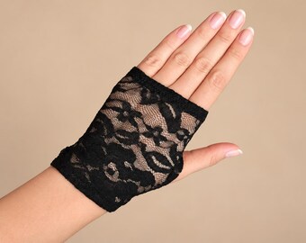 Könnte beinhalten: Ein schwarzer fingerloser Handschuh aus floralem Spitzenstoff. Das Accessoire bedeckt den Handrücken und das Handgelenk, verfügt über einen gewellten Rand oben und unten sowie eine Öffnung für den Daumen und ein offenes Handflächendesign.