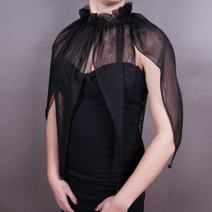 May include: A black sheer cape with a high ruffled collar and long sleeves. The cape is made of a delicate, lightweight fabric and has a flowing, elegant silhouette.