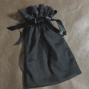 May include: A black mesh drawstring bag with a black ribbon and lace trim.