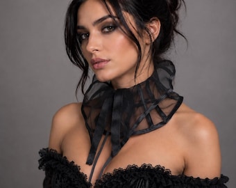 May include: A black sheer organza neck ruff featuring a structured collar design with ribbon ties, worn over a black off-the-shoulder lace corset top with scalloped trim and visible front hook-and-eye closures, creating a layered dark aesthetic.