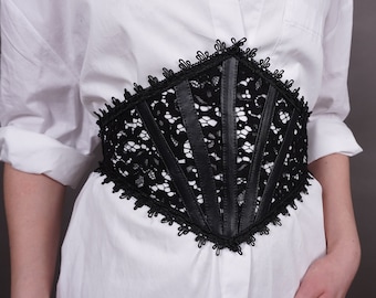 May include: A black lace corset belt with a leather center panel. The belt is worn over a white shirt.