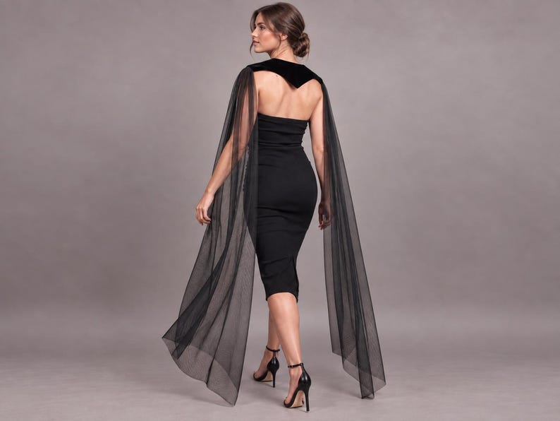 May include: A black strapless midi dress featuring a fitted silhouette and a velvet bodice overlay. The garment includes long, sheer black tulle cape sleeves that drape from the shoulders, extending down to the hemline of the dress.