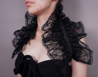 May include: A black lace collar with multiple ruffles. The collar is worn around the neck and shoulders.