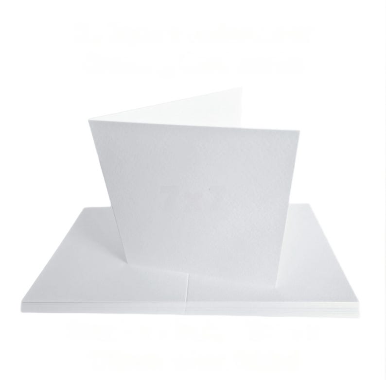 May include: A stack of white blank greeting cards with a folded card on top. The cards are made of textured paper and are set against a white background. The folded card is open, revealing the inside.