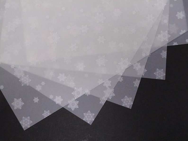May include: Four sheets of white tissue paper with a snowflake pattern. The tissue paper is translucent and the snowflakes are visible through the layers.