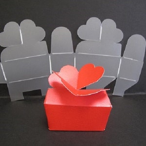 May include: A red heart-shaped box with a white paper template for making a similar box. The template is folded and shows the shape of the box.