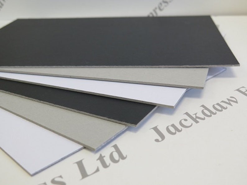 May include: A stack of five sheets of craft foam in various colors, including black, gray, and white. The foam is smooth and has a slightly textured surface. The foam sheets are arranged in a fan shape, with the black sheet on top and the white sheet on the bottom.