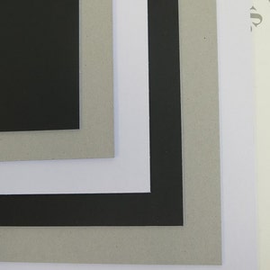 May include: Four pieces of cardboard in different colors and textures. The top piece is black, the second piece is gray, the third piece is white, and the bottom piece is white.