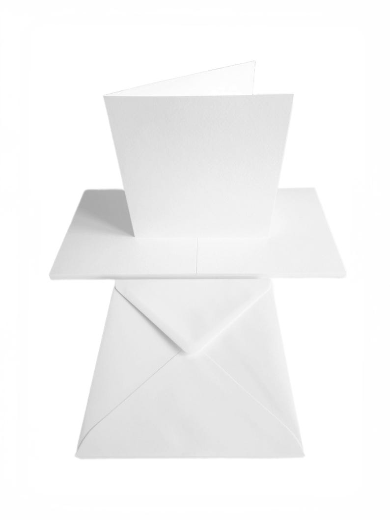 May include: A blank white greeting card, partially opened, with a matching white envelope. The card is rectangular and folded in half, with a clean, minimalist design. The envelope is sealed and positioned below the card.