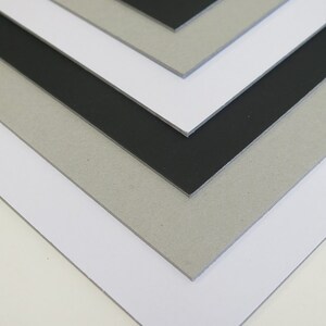 May include: Stack of four different colored sheets of cardboard. The top sheet is black, the second sheet is gray, the third sheet is white, and the bottom sheet is off-white.