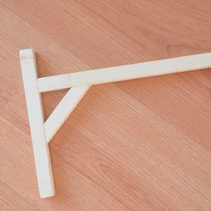 Può includere: Un supporto per mensola in legno con un supporto triangolare e un gancio in metallo all'estremità.