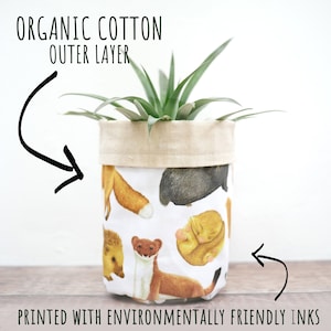 May include: A fabric plant pot featuring a woodland animal pattern on a white background. The pot has a natural canvas top and holds a green plant. Text reads "ORGANIC COTTON OUTER LAYER" and "PRINTED WITH ENVIRONMENTALLY FRIENDLY INKS".