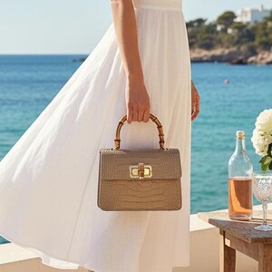 Puede incluir: Un vestido midi blanco de manga corta con escote en V, combinado con un sombrero de paja de ala ancha y un bolso beige estructurado con asa de bamb&uacute; y herrajes dorados. El vestido presenta una cintura entallada y una falda con vuelo.
