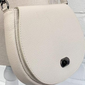 Bolso bandolera pequeño de piel color crema, estilo cartero.