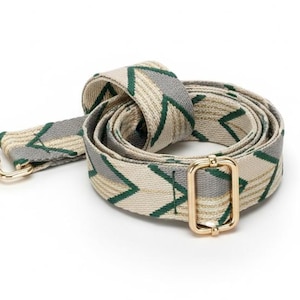May include: A coiled adjustable bag strap featuring a woven pattern of beige, grey, and dark green chevron lines. The strap includes gold-toned metal hardware, specifically a lobster clasp at one end and a rectangular sliding buckle for length adjustment.