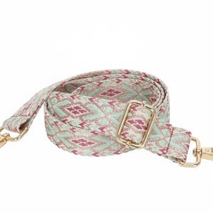May include: A woven bag strap featuring a repeating geometric pattern in shades of mint green, cream, and magenta. The strap includes gold-toned metal hardware, including a sliding adjuster and two swivel lobster claw clasps at each end.
