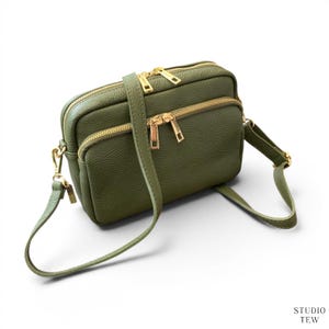 Peut inclure: Un sac bandoulière rectangulaire vert olive à la surface texturée, doté de deux compartiments principaux zippés avec des fermetures dorées. Le sac comprend une bandoulière réglable assortie fixée par des clips métalliques dorés.