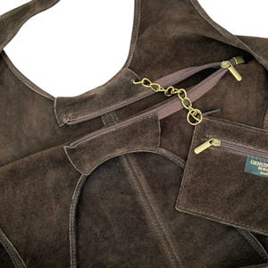 K&ouml;nnte beinhalten: Eine dunkelbraune Hobo-Tasche aus Wildleder mit Rei&szlig;verschluss oben, einer goldfarbenen Metallkette und einer passenden abnehmbaren Rei&szlig;verschlusstasche. Die Tasche enth&auml;lt ein kleines rechteckiges Etikett mit dem Text GENUINE BORS MADE.