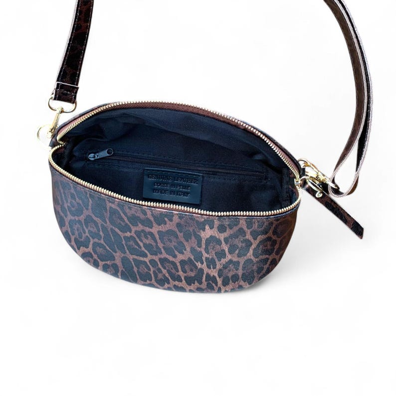 Puede incluir: Un bolso bandolera en forma de media luna con estampado de leopardo en tonos marr&oacute;n y negro. El bolso cuenta con una cremallera dorada, una correa ajustable a juego y un forro interior negro con una etiqueta de cuero Genuine Leather Made in Italy.