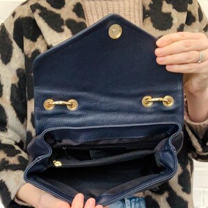 May include: A navy blue leather handbag with a gold zipper and gold hardware. The bag is open and the inside is visible.