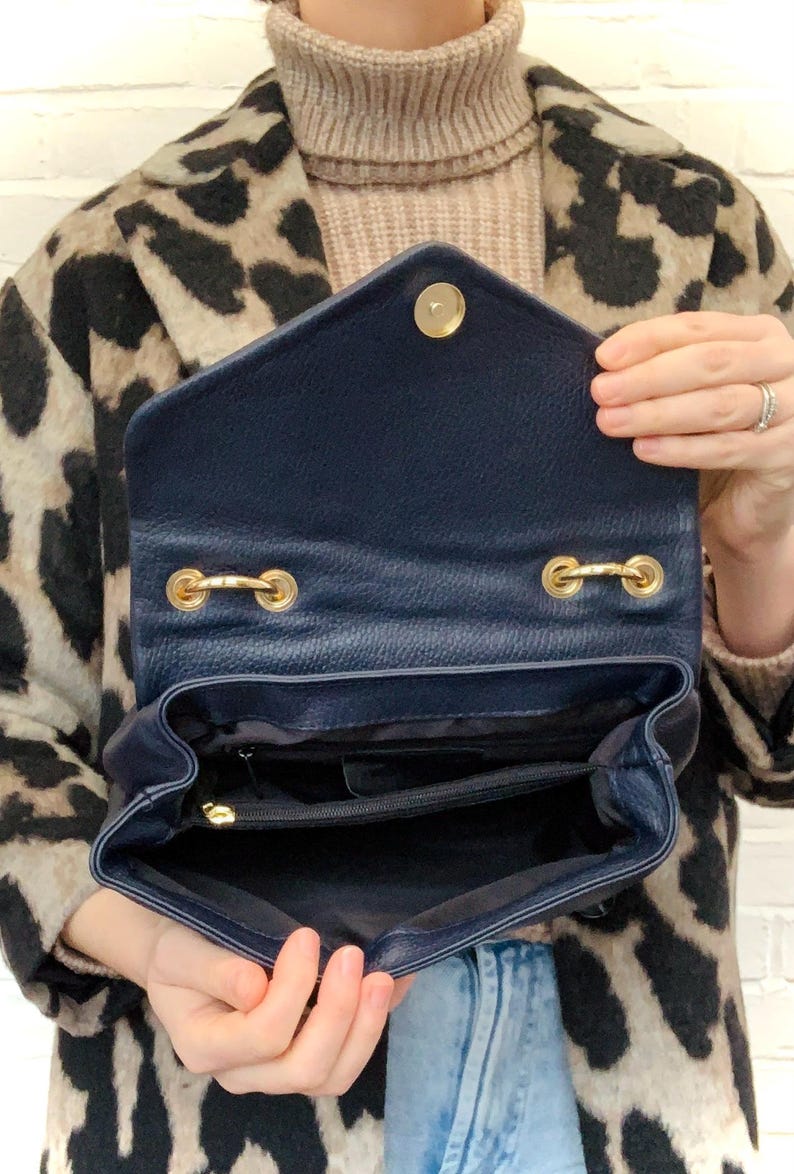 May include: A navy blue leather handbag with a gold zipper and gold hardware. The bag is open and the inside is visible.
