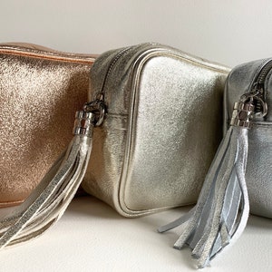 Puede incluir: Tres pequeños bolsos de bandolera metálicos con borlas. Los bolsos son de color oro rosa, plata y plata más claro.