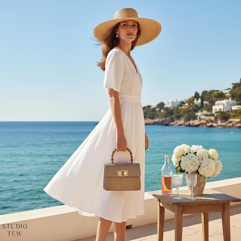 Puede incluir: Un vestido midi blanco de manga corta con escote en V, combinado con un sombrero de paja de ala ancha y un bolso beige estructurado con asa de bamb&uacute; y herrajes dorados. El vestido presenta una cintura entallada y una falda con vuelo.