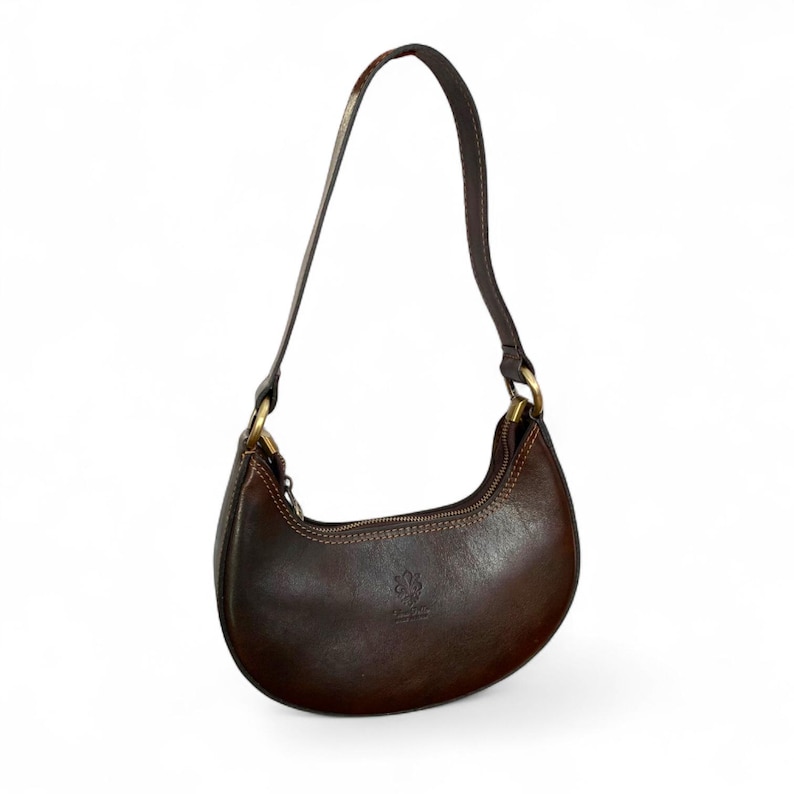 May include: A dark brown leather crescent-shaped shoulder bag with a smooth finish, featuring a single top handle attached with brass-toned metal hardware, a top zipper closure, and visible stitching along the edges of the curved body.