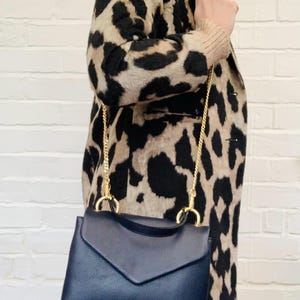 May include: A navy blue leather satchel bag with a gold chain strap. The bag has a flap closure and a small envelope-style pocket on the front.