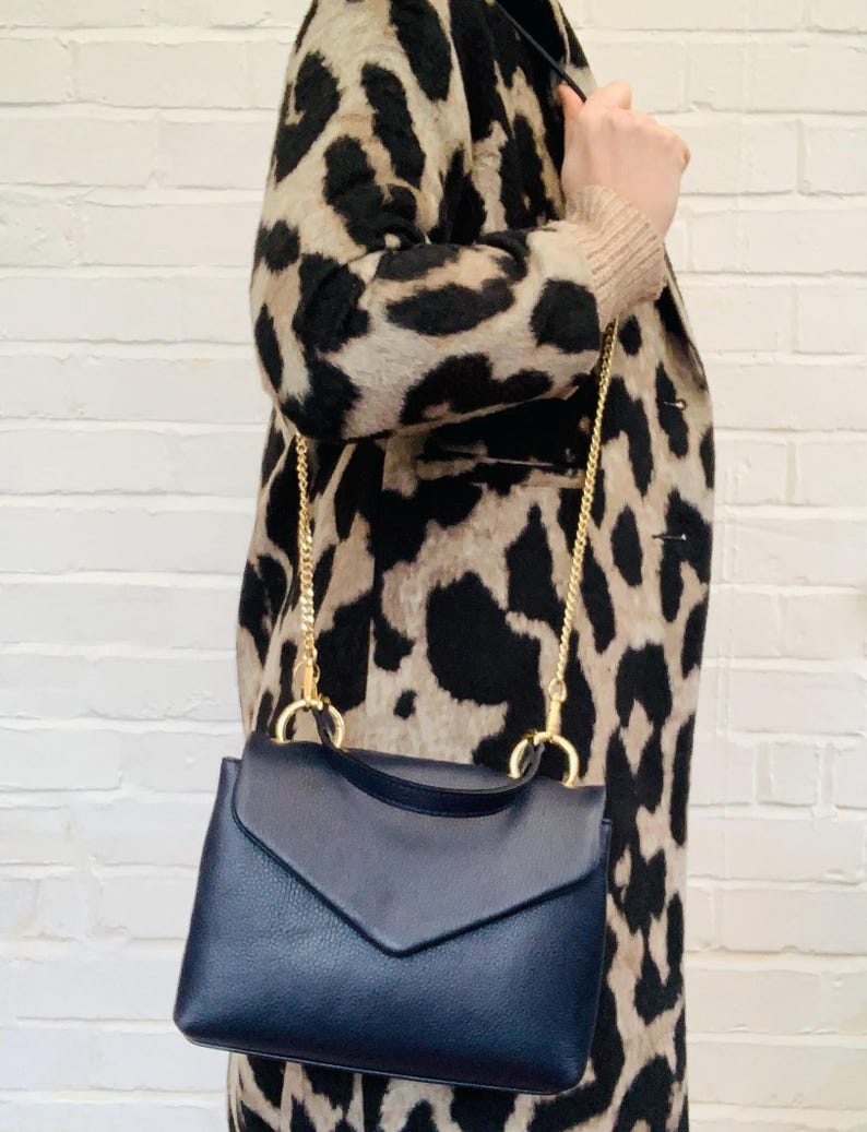 May include: A navy blue leather satchel bag with a gold chain strap. The bag has a flap closure and a small envelope-style pocket on the front.