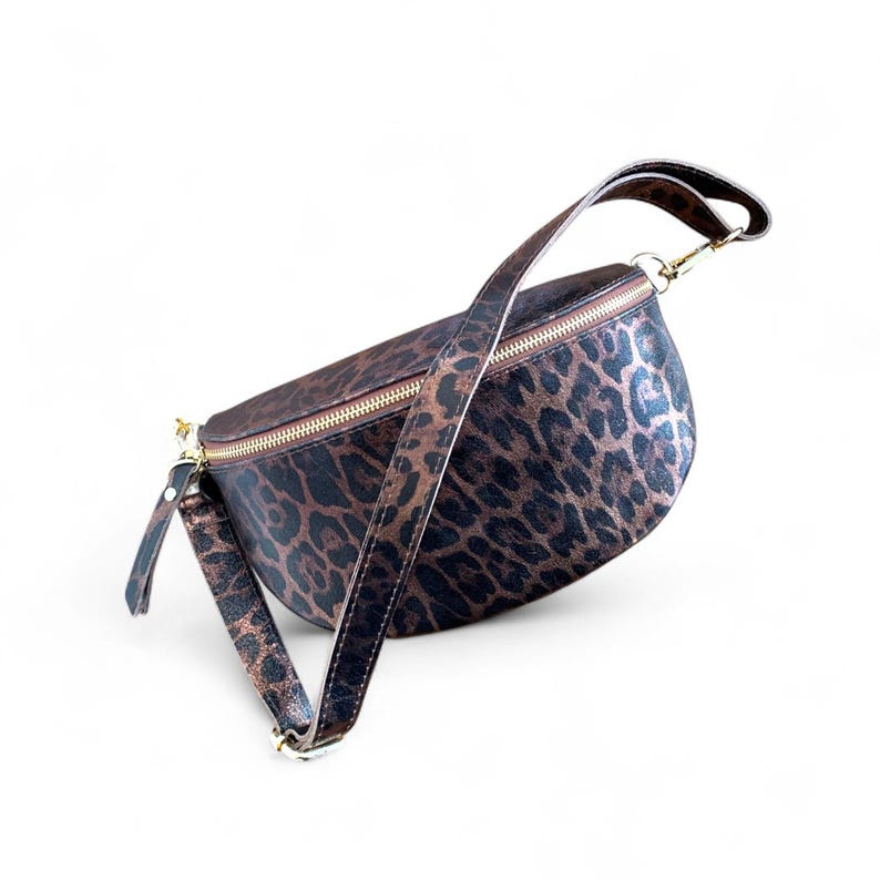 Puede incluir: Una ri&ntilde;onera en forma de media luna con un estampado de leopardo en tonos marr&oacute;n oscuro y negro. El bolso incluye un cierre de cremallera met&aacute;lico en tono dorado en la parte superior y una correa ajustable a juego con herrajes dorados.