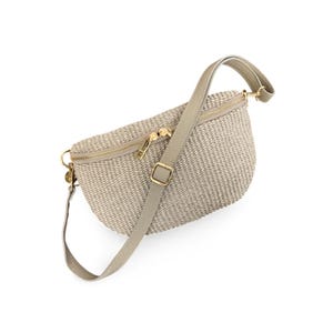 May include: A beige woven crossbody bag with a crescent shape, featuring a gold-tone zip closure and an adjustable strap. The bag has a textured, straw-like exterior finish and includes gold metal hardware accents on the strap and zip pull.