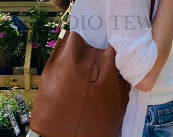 May include: A brown leather shoulder bag with a gold-colored clasp and strap. The bag is a medium size and has a simple, elegant design. The bag is being carried over the shoulder.