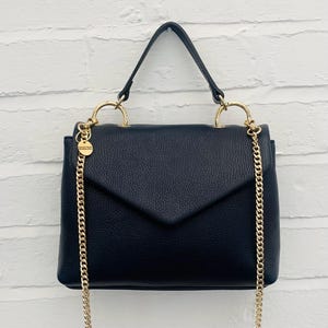 May include: A black leather satchel handbag with a gold chain strap and gold hardware. The bag has a flap closure and a top handle.