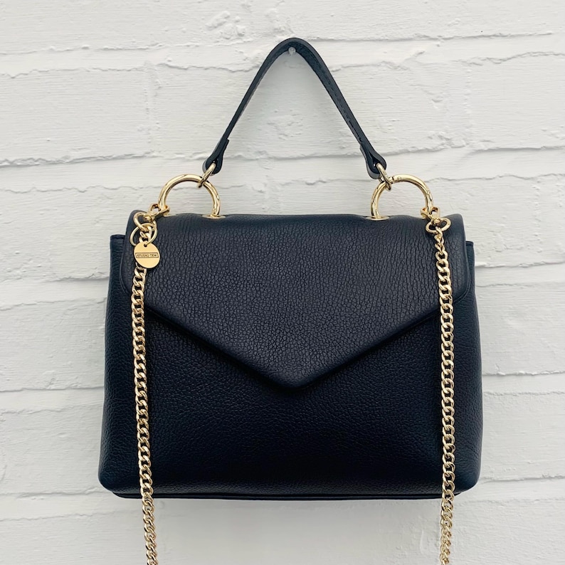 May include: A black leather satchel handbag with a gold chain strap and gold hardware. The bag has a flap closure and a top handle.