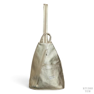 Puede incluir: Una mochila de cuero dorado metalizado con silueta triangular, un asa superior y cierre de cremallera vertical. La parte frontal incluye un bolsillo pequeño con una etiqueta plateada VERA PELLE MADE IN ITALY, con un acabado texturizado.