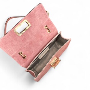 Puede incluir: Un bolso de mano de ante rosa empolvado con solapa rectangular, que presenta un inserto de asa de metal dorado, herrajes de cadena dorados y un cierre giratorio estilo bamb&uacute;. El interior est&aacute; forrado con un material claro y tiene una etiqueta.