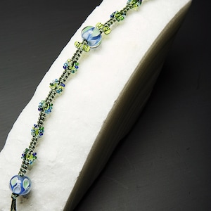 May include: A green and blue beaded bracelet with a larger blue and white glass bead in the center.