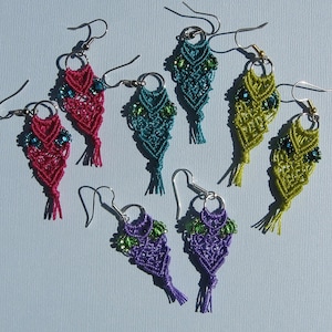 Könnte beinhalten: Ein Set mit zehn Eulen-Ohrringen aus buntem Makramee und grünen Perlen. Die Ohrringe sind in verschiedenen Farben, darunter Pink, Türkis, Lila und Grün.