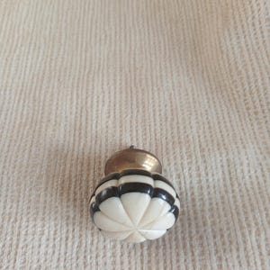 May include: A decorative cabinet knob with a carved, ivory-colored base and alternating black stripes. The knob has a brass-colored metal top. The knob is designed for furniture and home decor.