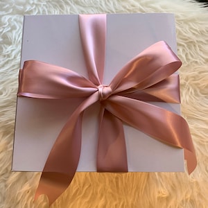May include: A white gift box with a large, blush pink satin ribbon tied in a bow.