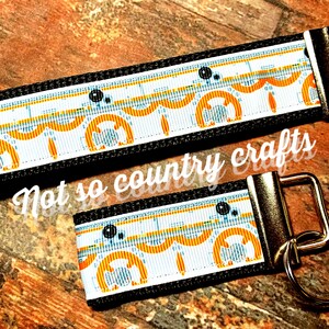 May include: Two keychains with a white, orange, and blue pattern featuring a repeating design of a robot head. The keychains are attached to gold metal key rings.