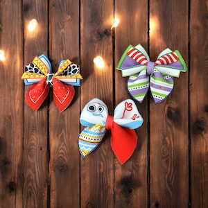 May include: Three fabric bow ties with different patterns. The first bow tie is red, yellow, and blue with a white polka dot pattern. The second bow tie is blue, white, and green with a striped pattern. The third bow tie is white with a blue and red pattern.