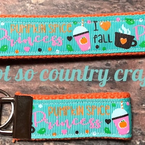 May include: A teal and orange key chain with a silver key ring. The key chain has a pattern of fall-themed images and the text "Pumpkin Spice Princess" and "I fall".