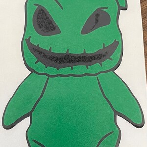 Pode incluir: Personagem de desenho animado verde com uma boca costurada e olhos pretos. O personagem est&aacute; de p&eacute; com os bra&ccedil;os ao lado do corpo.