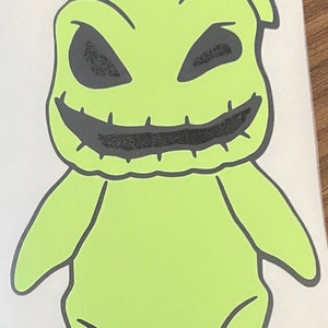 Pode incluir: Um personagem de desenho animado verde com a boca costurada e olhos pretos. O personagem est&aacute; de p&eacute; com os bra&ccedil;os ao lado do corpo.
