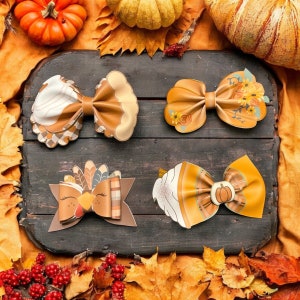 May include: Four handmade fabric hair bows with a fall theme. The bows are decorated with fall colors and designs, including pumpkins, turkeys, and leaves.
