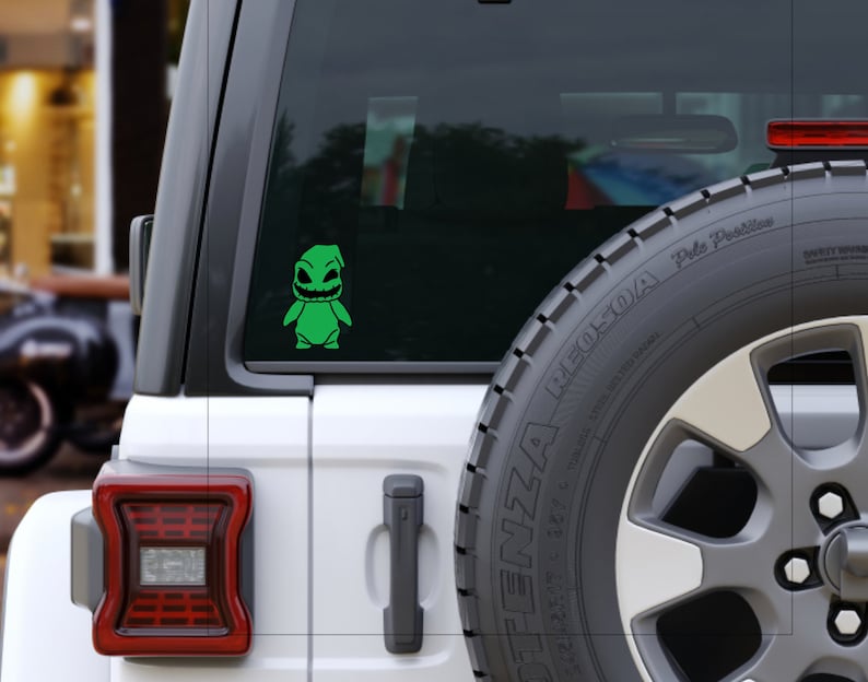 Pode incluir: Um Jeep branco com um adesivo de vinil verde de um personagem de desenho animado na janela traseira. O personagem tem um corpo verde, olhos pretos e uma boca preta. O adesivo est&aacute; na janela traseira do Jeep.