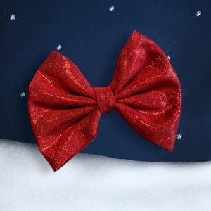 Puede incluir: Un gran lazo rojo brillante con un nudo central. El lazo está sobre un fondo azul oscuro con copos de nieve blancos.