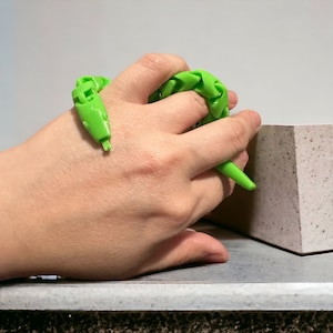 May include: A bright green, flexible, plastic snake toy. The snake is coiled and being held in a person's hand.